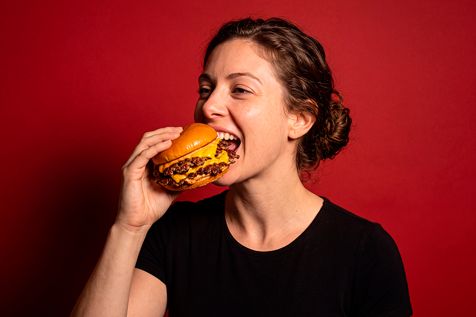 Woman taking a bite of a cheeseburger against a dark background